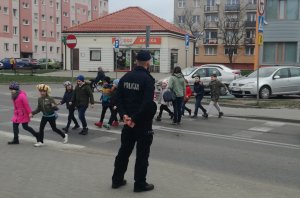 Policjant stojący przy przejściu dla pieszych przez które przechodzą dzieci