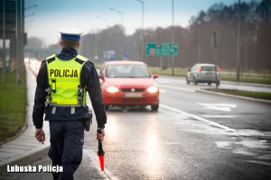 policjant ruchu drogowego stojący przy drodze obok niego przejeżdża pojazd