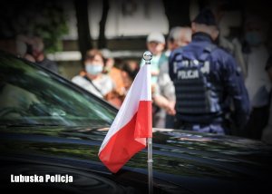 flaga Rzeczypospolitej, na drugim planie Policjant odwrócony plecami