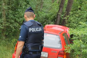 policjant na tle pojazdu pozostawionego w lesie
