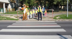 dzieci, policjantka i maskotka policyjna rozglądają się przed przejściem dla pieszych