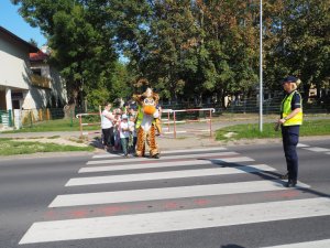 dzieci razem z maskotką policyjną przechodzą przez przejście dla pieszych
