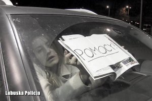 kobieta siedząca w samochodzie, która trzyma w ręku plakat z napisem pomocy