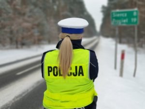 Policjantka stojąca tyłem do zdjęcia. w tle zaśnieżona droga .Warunki zimowe