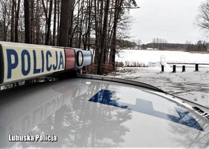 napis policja umieszczony na gondoli policyjnego radiowozu w tle zamarznięte jezioro pokryte śniegiem. Aura zimowa