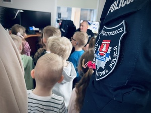 ramię policjanta w mundurze z logo jednostki w tle dzieci